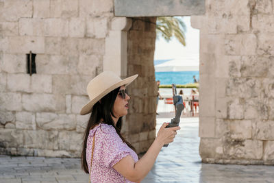 Side view of young woman using gimbal and mobile phone for vlogging on her travels.