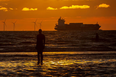 Silhouette another place statue at crosby beach in sea against sky during sunset