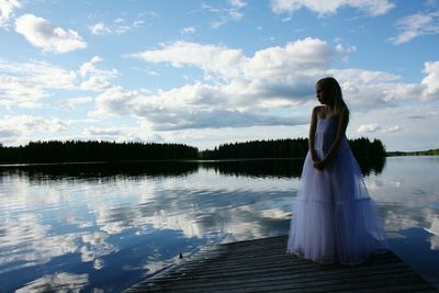 Girl in gown standing on pier by calm lake