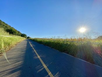 Road amidst field against blue sky