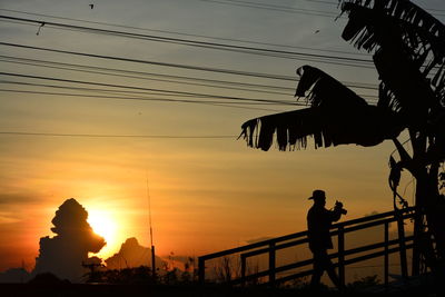 Silhouette people on electricity pylon against sky during sunset