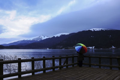 Rear view of man looking at pier over lake against sky