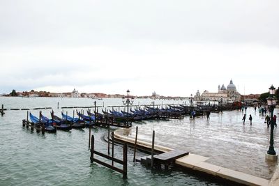 Boats moored in river by city against sky