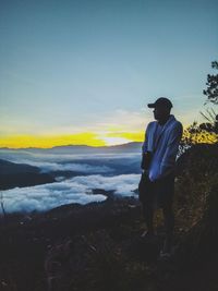 Silhouette man standing on landscape against sky at sunset