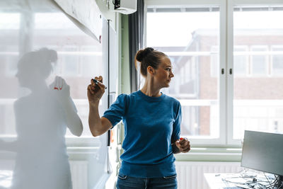 Female professor holding felt tip pen while standing near whiteboard in classroom at school