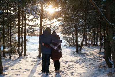 Couple standing in the winter forest looking on sunset near the frozen