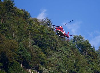 Low angle view of rescue helicopter over forest against sky 