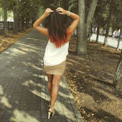 Rear view of young woman standing on footpath against tree