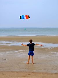 Rear view of boy playing on beach against clear sky