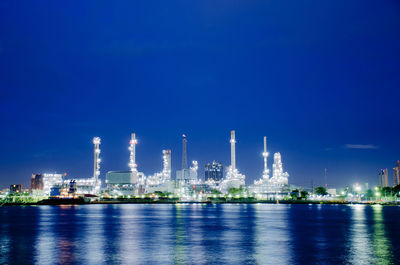 Illuminated factory against blue sky at night