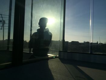 Silhouette man standing by glass window in city