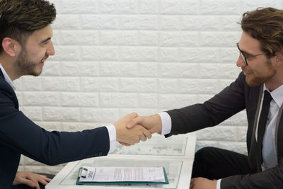 Businessmen shaking hands while sitting at table in office