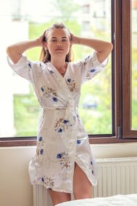 Portrait of a young woman standing against window