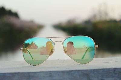 Close-up of sunglasses on retaining wall with reflection of man photographing