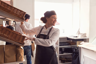 Happy female owner looking away while standing by shelves in brightly lit grocery store