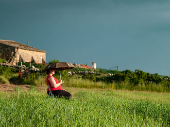 Woman with umbrella sitting on field against clear sky