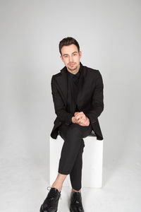 Portrait of young man sitting against wall