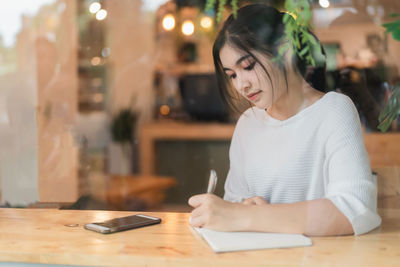 Young woman using mobile phone while sitting on table