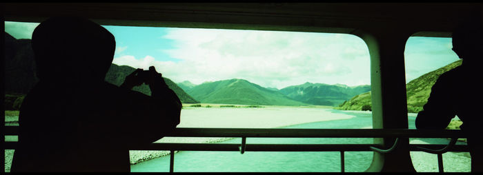 Silhouette people by window against mountains