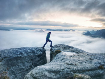 Male hiker finnaly standing on a rock stock and enjoying foggy mountain view