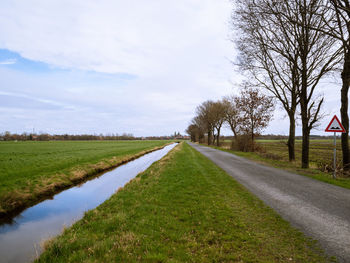 Empty road amidst field against sky