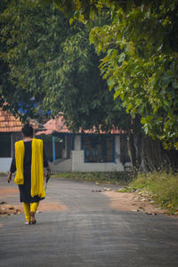 Rear view of woman walking on footpath amidst trees