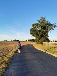 Rear view of man walking on road amidst field against sky