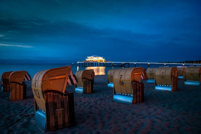 Hooded chairs on beach against sky at dusk