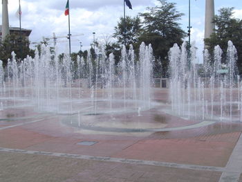 Fountain in city against cloudy sky