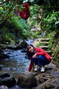 Portrait of young woman by rock in forest