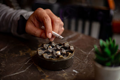 Cropped hand of man holding cigarette over ashtray on table