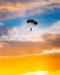 Low angle view of silhouette person paragliding against orange sky