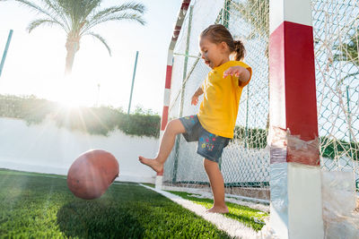 Cute little girl kicking soccer ball while standing in gateway