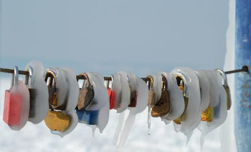 Close-up of frozen padlocks hanging on railing against sky during winter