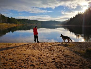 Rear view of man standing with dog on lake against sky