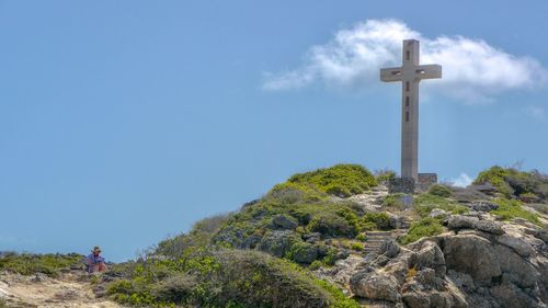 Low angle view of cross on rock against blue sky