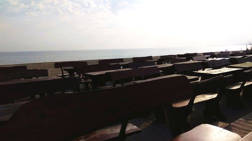 Empty chairs and tables at beach against sky