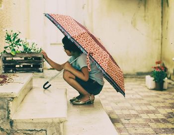 Side view of a girl holding umbrella on footpath