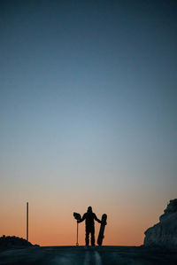 Silhouette man standing with snowboard against sky during sunset