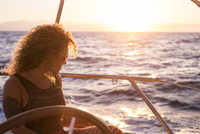 Side view of woman sitting on sailboat in sea