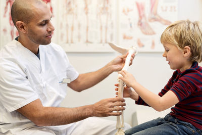 Male orthopedist explaining hand model to boy at clinic