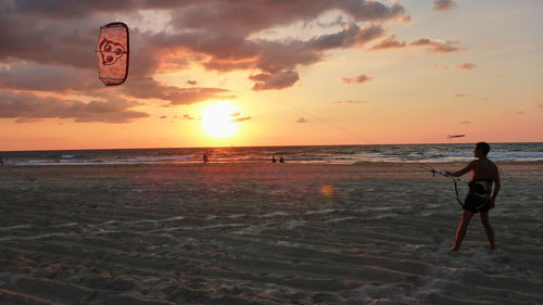 Man kiteboarding at beach against sky during sunset