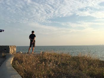 Rear view of man standing on field by sea against sky