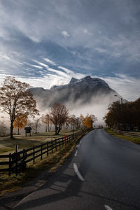 Picturesque rural road with mountains and mist in vanishing point.