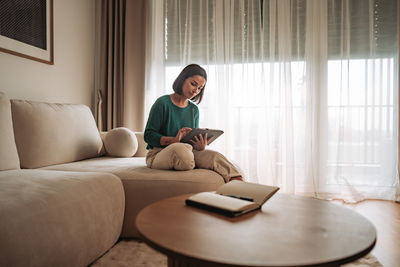 Young woman using mobile phone while sitting on bed at home
