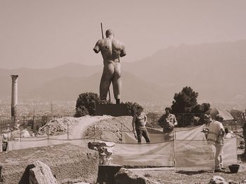 Men standing on sculpture against sky