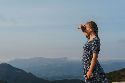 Side view of woman standing on mountain against sky