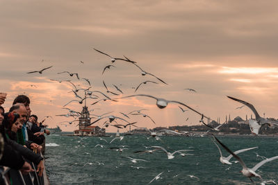 People by sea against sky during sunset