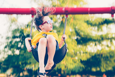 Low angle view of boy wearing sunglasses swinging outdoors