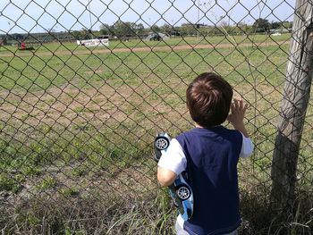 Rear view of boy standing by chainlink fence